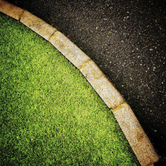 The vibrant green grass curves smoothly alongside a dark asphalt pathway, creating a pleasing contrast in an urban environmental setting during the daytime