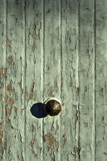 The image captures a close-up of a rustic doorknob on an old, weathered wooden door. The green paint is peeling, revealing the wood beneath, creating a textured and aged appearance