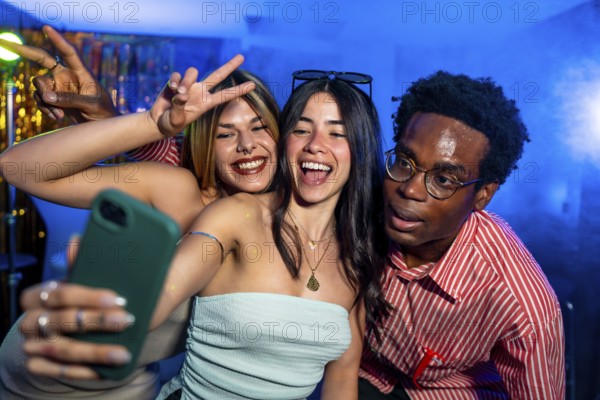Happy multi ethnic friends taking a selfie while partying in a nightclub, making peace signs and smiling