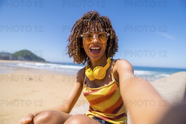 Happy young woman with headphones and sunglasses taking a selfie on a sunny beach, enjoying her summer vacation
