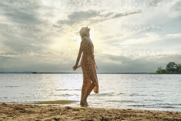 Woman enjoying serenity by the lakeside at sunset with vibrant dress flowing in the breeze