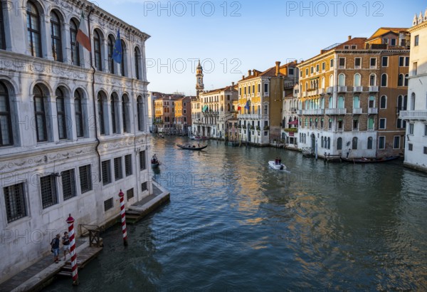 View of the Grand Canal with gondoliers at sunset, picturesque evening mood with palazzos on the canal and church tower of the Chiesa Parrocchiale dei Santi Apostoli, view from the Rialto Bridge, Venice, Veneto, Italy