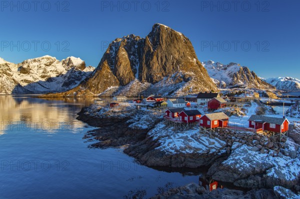 Fishermen's Village in front of snowy mountain range at the coastline in winter, Lofoten, Norway