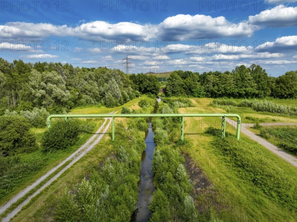 Bottrop, North Rhine-Westphalia, Germany - Renaturalised Boye, the tributary of the Emscher, has been transformed into a near-natural watercourse, flood protection through newly designed flooding areas, the Boye is now free of wastewater following the construction of a parallel sewer, is part of the Emscher river system and thus part of the Emscher conversion, was previously an open, above-ground wastewater channel, mixed water channel with surface water and wastewater. Wind turbine on the Mottbruch spoil tip at the back