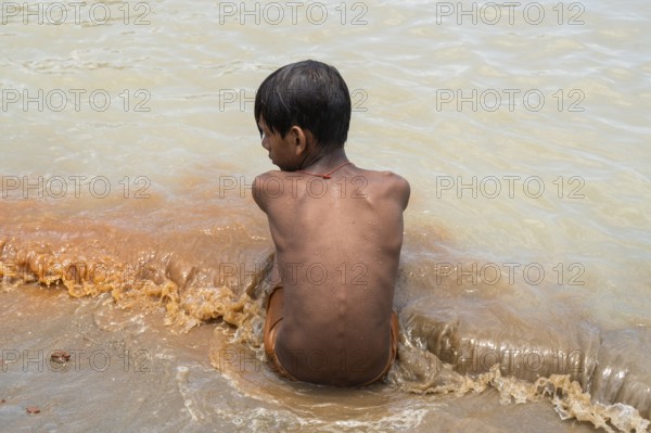 A boy sits in the bank of Brahmaputra River as he bathe to seek relief from the intense summer heat in Guwahati, India, on June 26, 2025