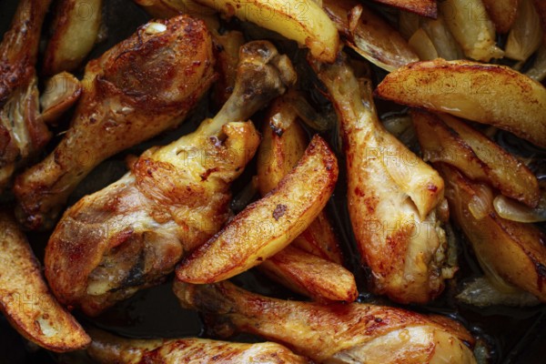 Fried chicken drumsticks with potato slices, in a clay pan, baked in the oven, with spices, homemade, no people