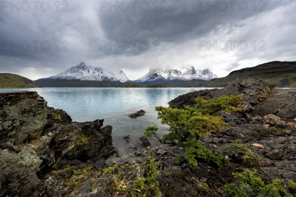 Cloudy mountain range Cuernos del Paine, shore of the blue lake Lago Pehoe in the evening light, dramatic sky, Torres del Paine National Park, Chile