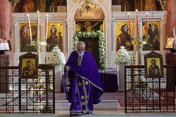 Priest in purple robe walking past an altar with icons and burning candles, Church of the Annunciation of the Blessed Virgin Mary, Rhodes Town, Greece, Orthodox Church, Dodecanese, Greek Islands, Rhodes Town, Holy Week, Rhodes