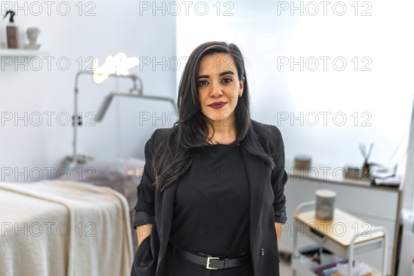 Young female beautician smiling in her beauty salon or hairdressing aesthetic center, wearing professional clothes and looking confident