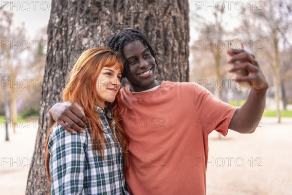 Interracial couple taking a selfie with a smartphone in a park, smiling and enjoying a moment together