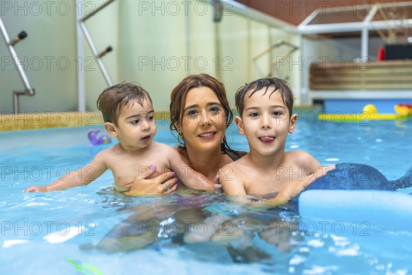 Happy mother embracing her two children while playing and smiling in a swimming pool during summer vacation