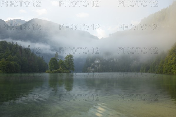 Mystical morning at Königssee in Schönau with boathouses and Christlieger. Sunrise and beautiful wafts of mist over the Königssee in the basin