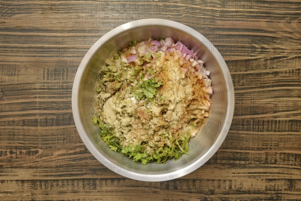 Overhead view of a bowl with chopped herbs, diced onions, and various spices added to minced meat