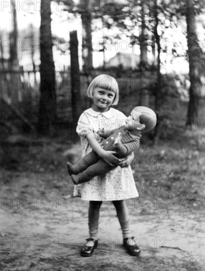 Girl with doll, 1930, Cheerful girl holding a doll in a wooded area on a sunny day, Historical photo