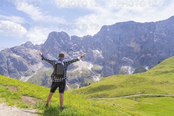 A hiker with raised arms looks at an impressive mountain scenery in a meadow, Alpe di Siusi, Dolomites, South Tyrol, Italy