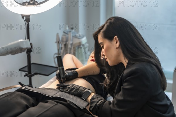 Beautician using a microneedling device, providing a cosmetic treatment to a client lying on a bed in a professional beauty salon