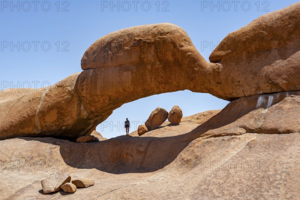 Tourist in a rock arch, round rock formations with stone arch, Pontok Mountains, Great Spitzkoppe, Spitzkoppe, Great Spitzkoppe Nature Reserve, Namibia