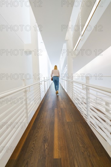 Woman walking along a modern corridor characterised by light-coloured walls and wooden flooring, Frieder Burda Museum, Baden Baden, Germany