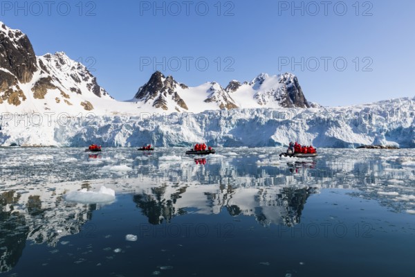 Group of Zodiacs in front of glacier and mountain range with snow, sea, Fugelfjorden, Spitsbergen, Svalbard