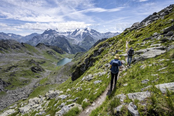 Mountaineer on hiking trail in mountain landscape, descent at Col du Louvie, view of mountain lake Lac du Louvie and glaciated mountain peaks of the Grand Combine, Valais Alps, Val de Bagnes, Valais, Switzerland