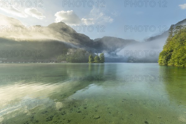 Mystical morning at Königssee in Schönau with boathouses and Christlieger. Sunrise and beautiful wafts of mist over the Königssee in the basin
