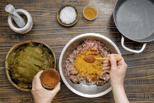 Home cook prepares dolma by adding pepper mix into minced meat. Pickled grape leaves are ready for wrapping, creating a traditional Georgian dish with rich flavors
