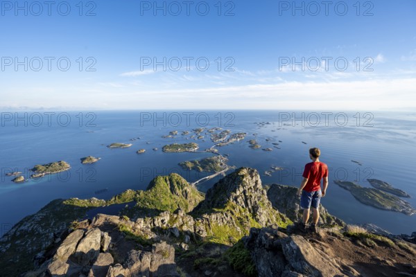 View of numerous small rocky islands with houses, mountaineers on the summit of Festvågtind, view of Henningsvær, Vågan, Lofoten, Nordland, Norway