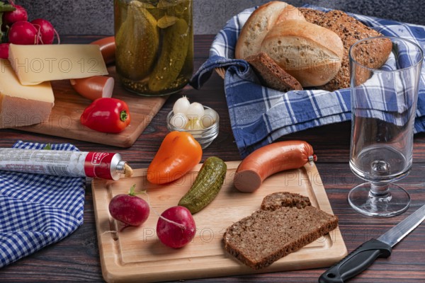 Rustic arrangement with sausage, cheese, vegetables, mustard and bread on a laid table