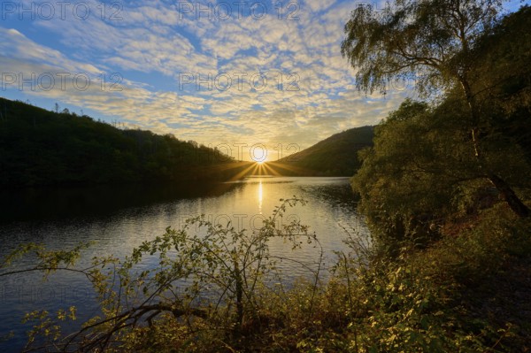 The sun sinks behind hills on the lake, golden glow and reflecting water surface, summer, Rursee, Obersee, Simmerath, Eifel National Park, North Rhine-Westphalia, Germany