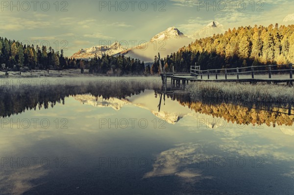 Lake Staz near Sankt Moritz in the Engadin in Switzerland. Morning atmosphere with fog in autumn. Water reflection and snow-covered mountains in the background