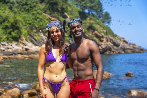 Interracial couple smiling and wearing snorkeling gear at a beautiful beach getting ready to snorkel