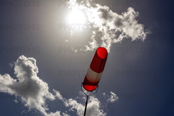 A colorful windsock hangs from a tall pole, clearly indicating wind direction. The bright sky is filled with scattered clouds, creating a vivid backdrop during daytime