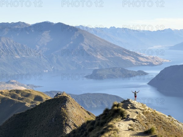 Person with outstretched arms on the hiking trail to Roys Peak Lookout, Lake Wanaka, Wanaka, South Island, New Zealand, Oceania