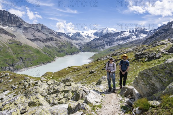 Mountaineer on a hiking trail at a blue mountain lake, reservoir Lac des Dix, behind mountain peak Mont Blanc de Cheilon, Hérménence, Valais Alps, Valais, Switzerland