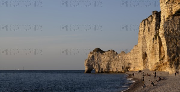 People on the beach, pebble beach, rock arch Falaise or Porte d'Amont, Étretat, sea, steep coast, cliffs, chalk cliffs, alabaster coast, La Côte d'Albâtre, evening mood, atmospheric, Normandy, Seine-Maritime, France