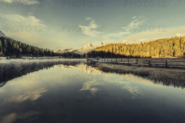 Lake Staz near Sankt Moritz in the Engadin in Switzerland. Morning atmosphere with fog in autumn. Water reflection and snow-covered mountains in the background