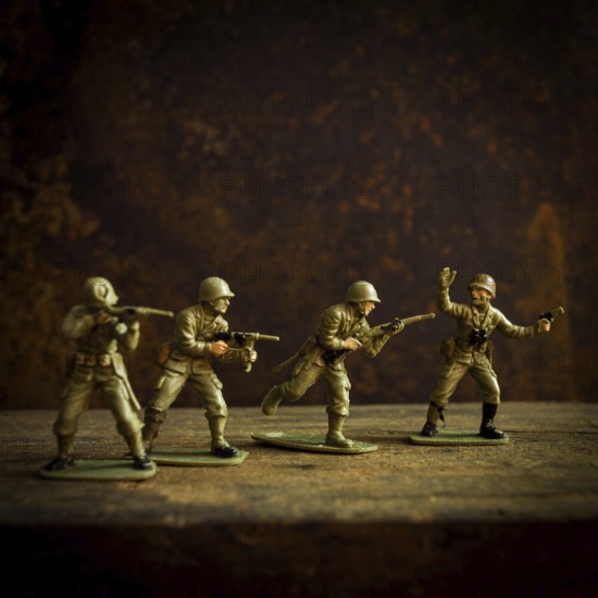 Four toy soldiers stand in various combat stances, ready for action on a weathered wooden surface. The dark background enhances their vintage military theme