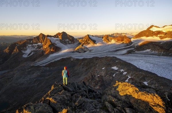 Mountaineer in front of picturesque high mountain landscape at sunrise with alpenglow, glacier and rocky mountain peaks in the morning light, view at the Becher on mountain peaks Königshofspitz and Sonklarspitze and Schwarzwandspitz with glacier Übeltalferner, Stubai Alps, South Tyrol, Italy
