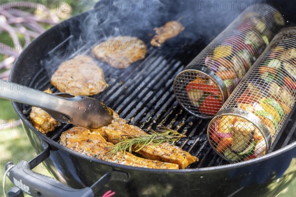 Barbecue in the garden. Meat and vegetables, vegetarian and vegan, are served on the kettle grill. Barbecue baskets for gently braising carrots, courgettes or peppers are right on trend. Münsingen, Baden-Württemberg, Germany