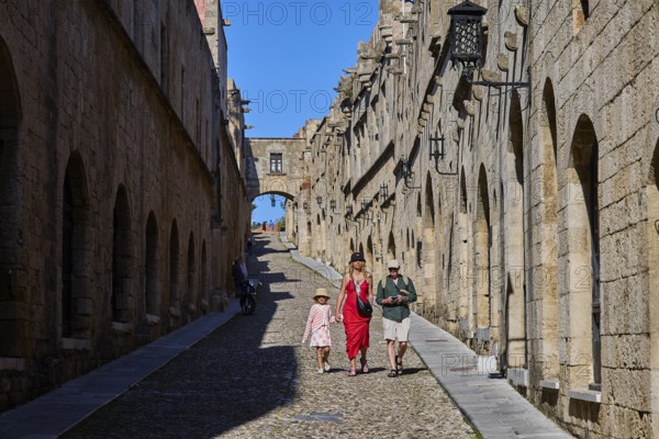 Tourists walking through a sunny, stony alley, Knights Street, Rhodes Old Town, Rhodes, Dodecanese, Greek Islands, Greece