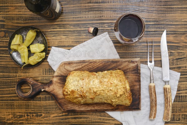 Delicious homemade roasted pork meat and pickled peppers on a rustic wooden table surrounded with red wine in glass, while utensils and a cloth, creating a warm atmosphere for dining