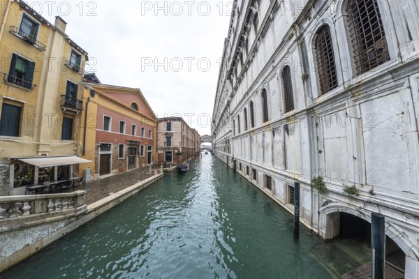 Serene canal in venice with traditional gondola navigating towards distant bridge, showcasing colorful buildings and historic architecture