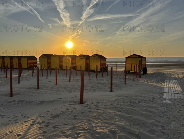 Beach huts at sunset with sand and sea in the background. The sky is streaked with clouds, De Panne, West Flanders, North Sea, Belgium