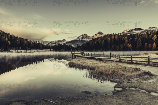 Lake Staz near Sankt Moritz in the Engadin in Switzerland. Morning atmosphere with fog in autumn. Water reflection and snow-covered mountains in the background