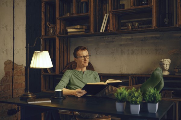 A person sits comfortably in a modern workspace, immersed in a book. Soft lamp light creates a warm atmosphere. Green plants and rustic shelves add character to the relaxing environment