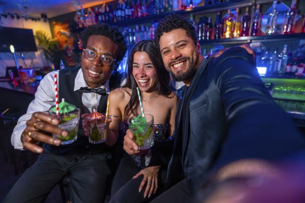 Three friends smiling and capturing a selfie while enjoying colorful cocktails at a lively bar, celebrating friendship and fun together