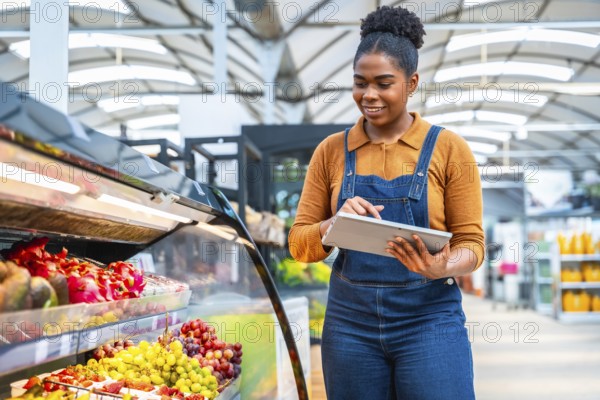 Smiling african supermarket employee using digital tablet checking products freshness and managing inventory in grocery store
