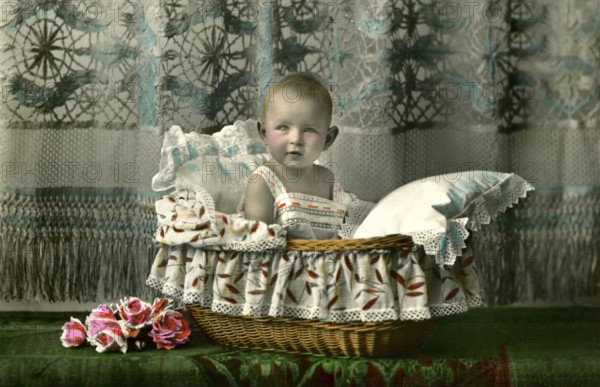 Baby in a basket, 1920s, A toddler sits cosily in a bassinet, surrounded by floral details, Historical photo