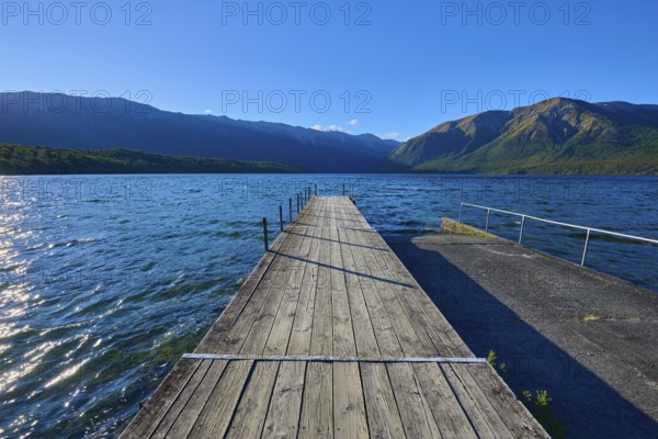 A wooden jetty stretches into a clear blue lake surrounded by majestic mountains, Summer, Lake Rotoiti, Saint Arnaud, Tasman Region, South Island, New Zealand