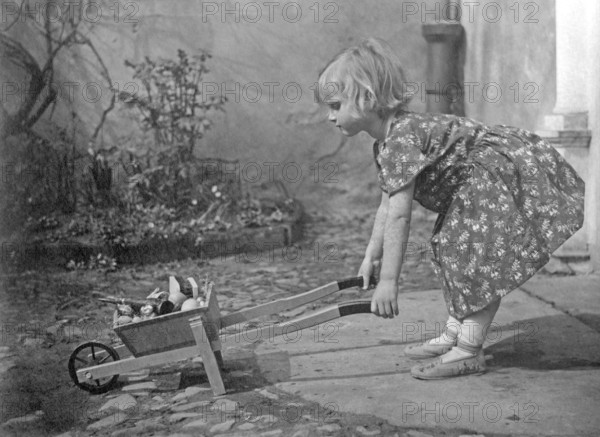 Girl with wheelbarrow, 1920s, A girl playing in the garden with a wheelbarrow, Historical photo